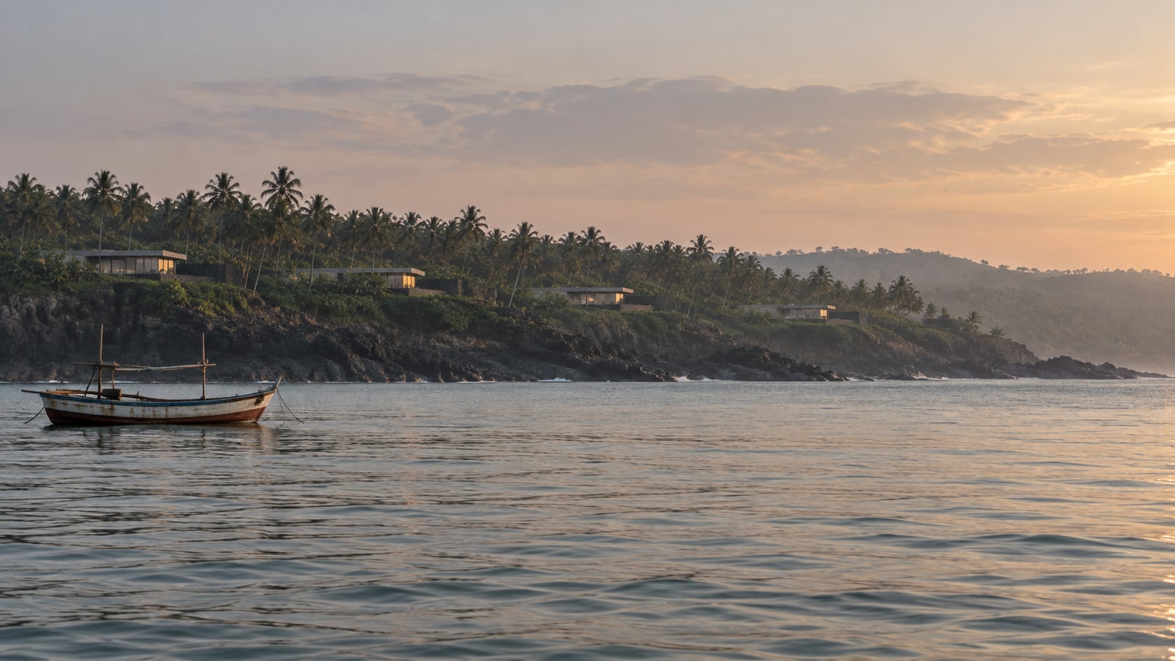 The basalt headland seen from the sea in early morning, five low houses among coconut palms and a fishing boat at anchor